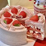 liced strawberry cream cake with fresh berries and pink frosting, branded Soi Sun, next to Hello Kitty themed cup.