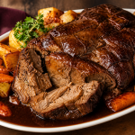 A succulent roast beef slice drenched in glossy rich gravy, served on a white plate with roasted potatoes and a sprinkle of fresh parsley, presented on a wooden surface.