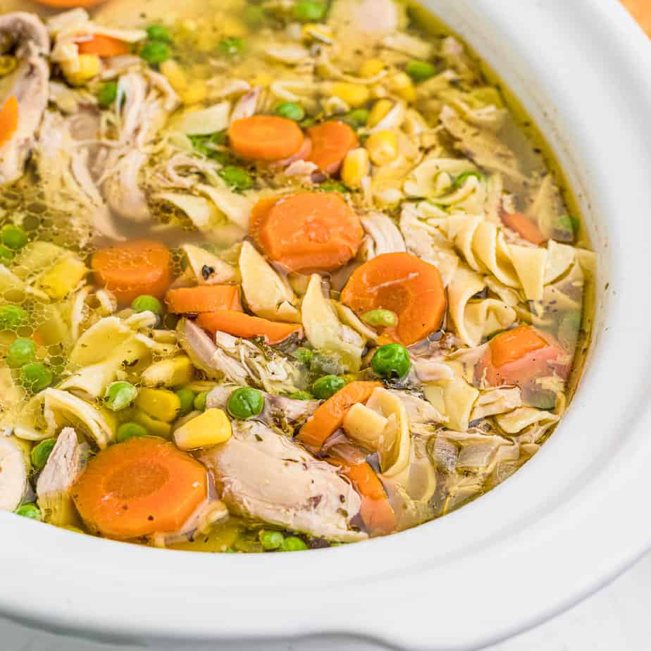 A steaming bowl of hearty chicken noodle soup filled with tender chicken pieces, sliced carrots, peas, corn, and delicate noodles in a golden broth. Served in a white bowl, showcasing its vibrant and fresh ingredients.