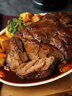 A succulent roast beef slice drenched in glossy rich gravy, served on a white plate with roasted potatoes and a sprinkle of fresh parsley, presented on a wooden surface.