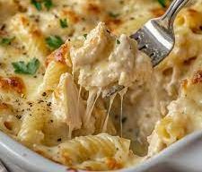 A white dish filled with creamy chicken pasta bake, featuring tender pasta and chicken chunks in a stretchy cheesy sauce, garnished with parsley and black pepper, with a fork lifting a portion.