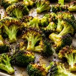 Close-up of crispy oven roasted broccoli florets on a baking sheet with golden charred edges and garlic seasoning.