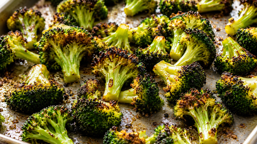 Close-up of crispy oven roasted broccoli florets on a baking sheet with golden charred edges and garlic seasoning.