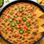 Creamy cheesy beef dip in a cast iron skillet topped with jalapeños, diced tomatoes, and cilantro, served with tortilla chips